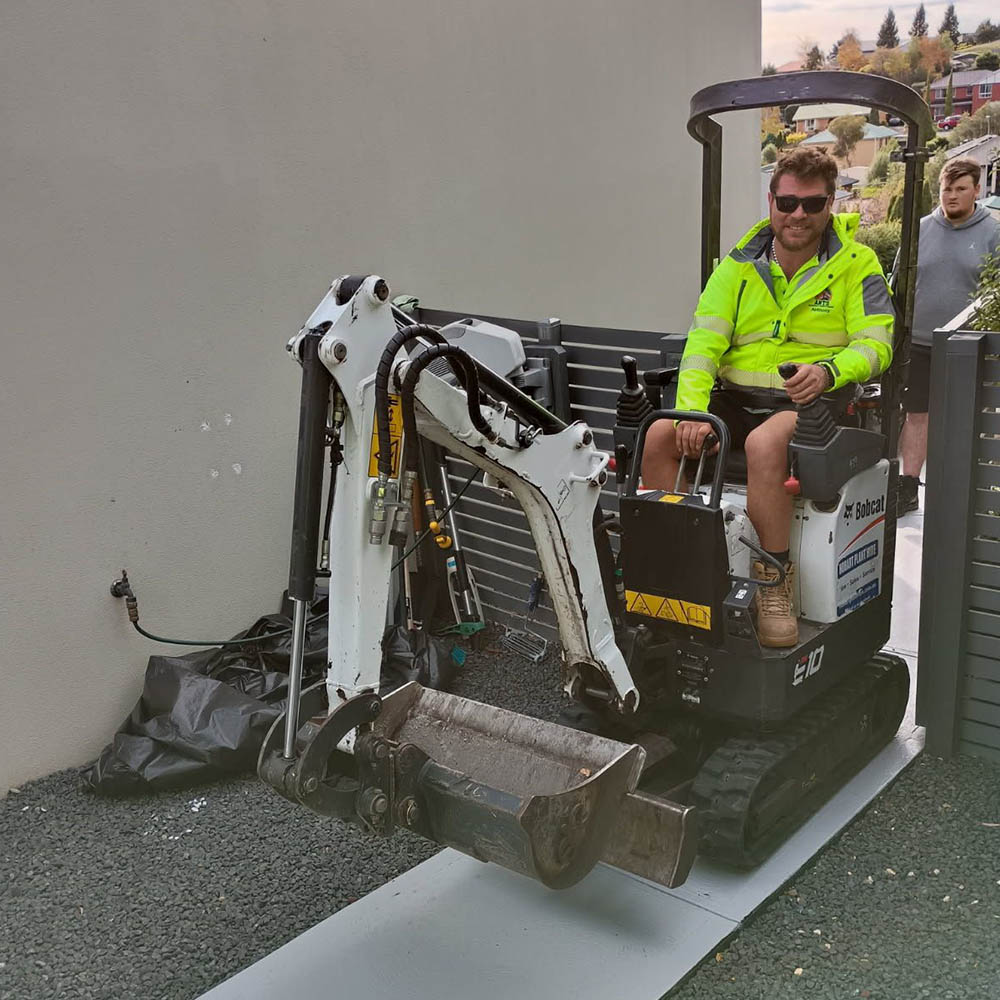 services4 Man in hi-vis driving a mini excavator on a board beside a house